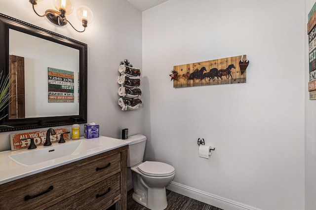 half bathroom with baseboards, vanity, and toilet