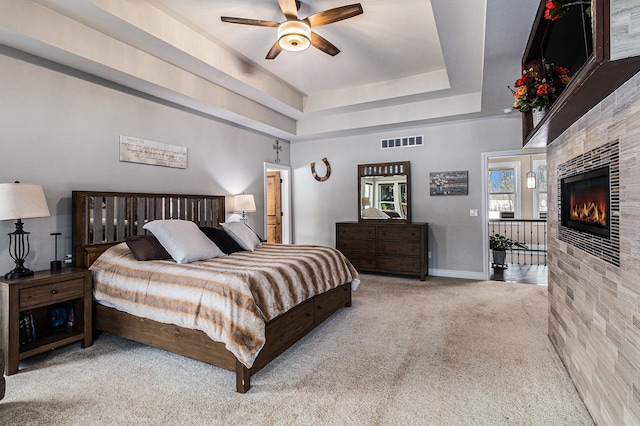 bedroom featuring baseboards, a raised ceiling, visible vents, a tile fireplace, and light colored carpet