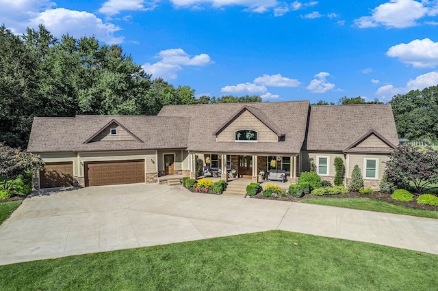 view of front facade featuring stone siding, a front yard, driveway, covered porch, and a garage