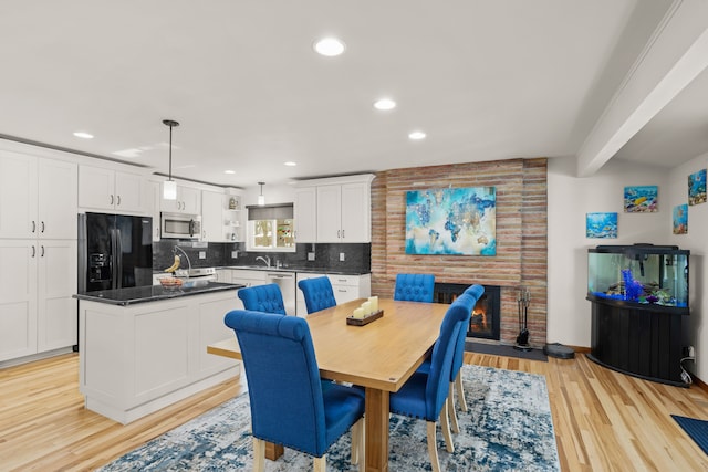 dining space with a brick fireplace, light wood-type flooring, beam ceiling, and recessed lighting