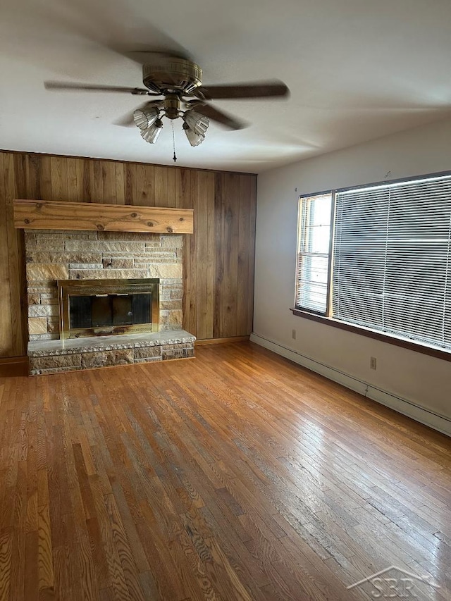 unfurnished living room with ceiling fan, a fireplace, light hardwood / wood-style flooring, and wood walls