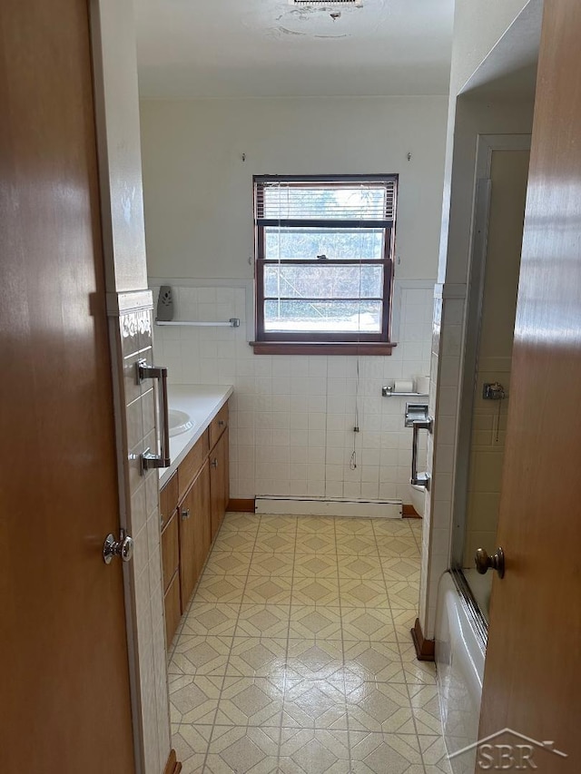 bathroom with a baseboard radiator, vanity, bath / shower combo with glass door, and tile walls