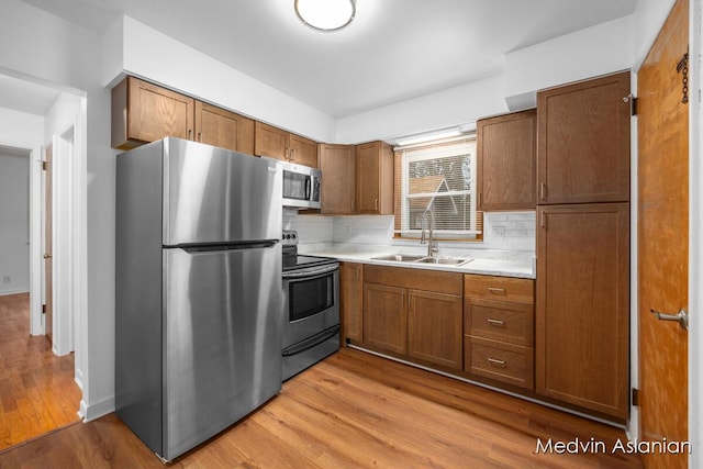 kitchen with appliances with stainless steel finishes, sink, decorative backsplash, and light wood-type flooring