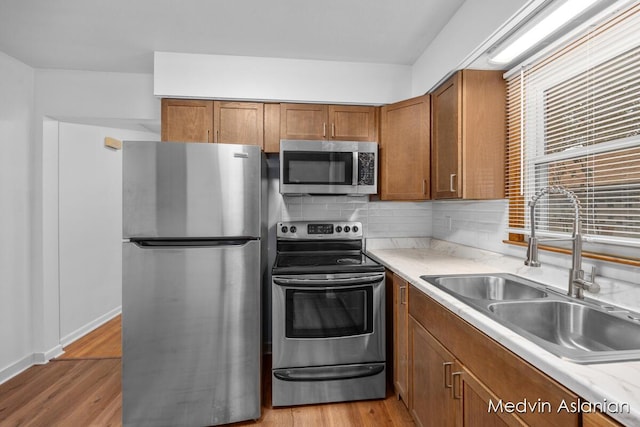 kitchen with appliances with stainless steel finishes, sink, backsplash, and light hardwood / wood-style floors