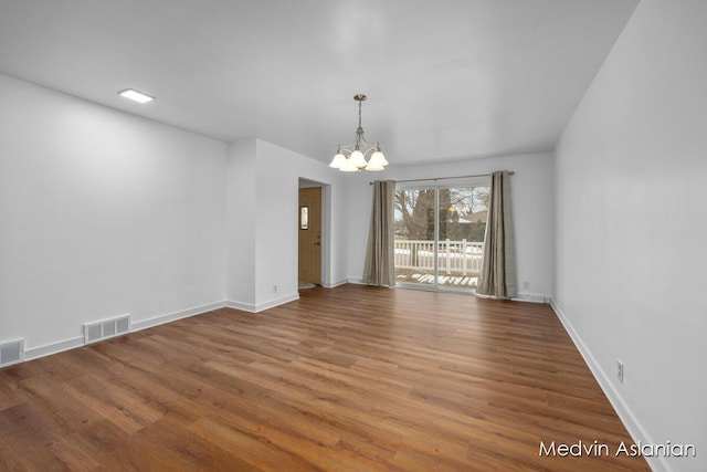 empty room with wood-type flooring and a chandelier