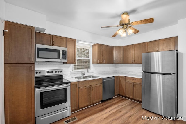 kitchen with sink, light wood-type flooring, appliances with stainless steel finishes, ceiling fan, and backsplash