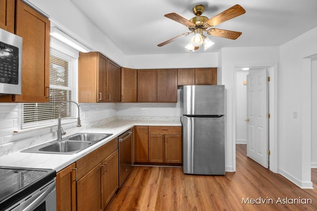 kitchen featuring appliances with stainless steel finishes, sink, backsplash, ceiling fan, and light wood-type flooring