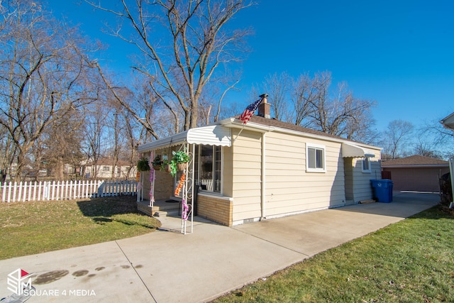 view of property exterior with brick siding, fence, a yard, a chimney, and a patio area