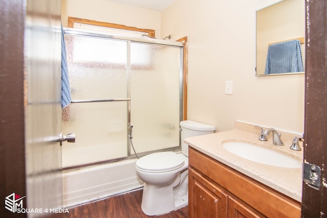 full bath featuring toilet, combined bath / shower with glass door, wood finished floors, and vanity