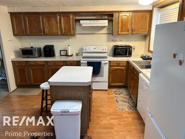 kitchen with sink, a center island, a kitchen breakfast bar, white appliances, and light hardwood / wood-style floors