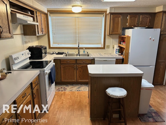 kitchen featuring sink, white appliances, a center island, light hardwood / wood-style floors, and a textured ceiling