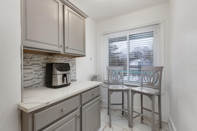 kitchen featuring tasteful backsplash, radiator heating unit, gray cabinets, and light stone countertops