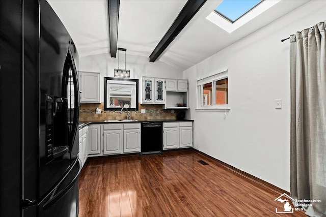 kitchen featuring dark hardwood / wood-style floors, vaulted ceiling with skylight, white cabinetry, sink, and black appliances