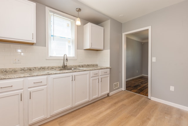 kitchen featuring sink, hanging light fixtures, white cabinets, light hardwood / wood-style floors, and backsplash