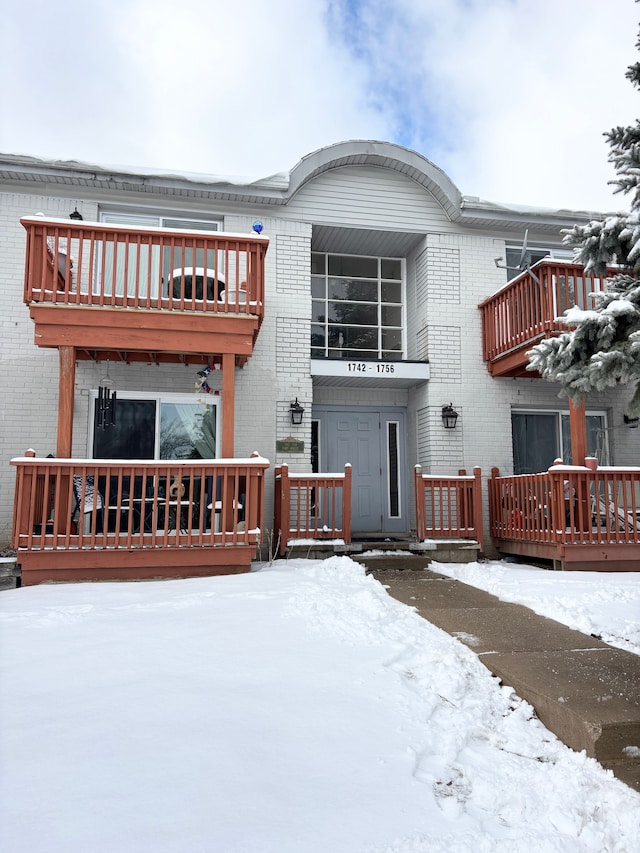 snow covered house featuring a balcony and brick siding