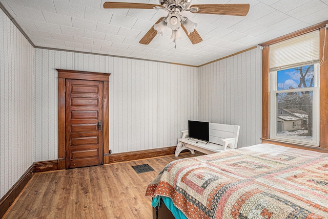 bedroom with wood finished floors, crown molding, baseboards, and wallpapered walls