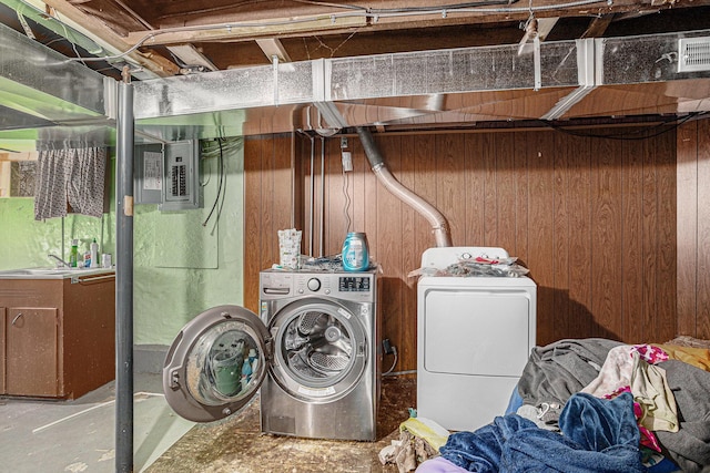 laundry room featuring washing machine and dryer, wood walls, a sink, laundry area, and electric panel