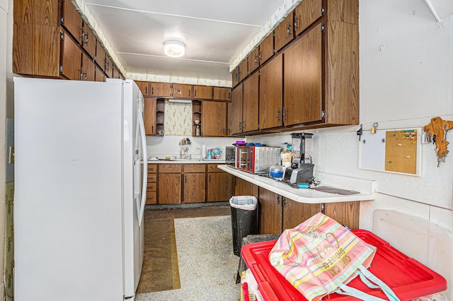 kitchen with brown cabinetry, light countertops, a sink, and freestanding refrigerator