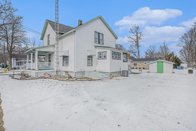 snow covered house with an outbuilding, a chimney, central air condition unit, a porch, and a shed