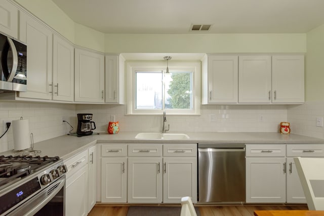 kitchen featuring decorative light fixtures, white cabinetry, stainless steel appliances, and sink