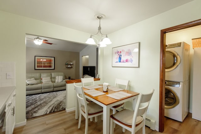 dining space with stacked washer / drying machine, lofted ceiling, light hardwood / wood-style flooring, a baseboard heating unit, and ceiling fan with notable chandelier