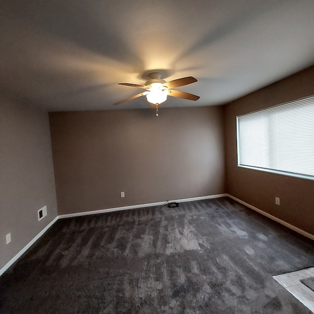 unfurnished room with dark colored carpet, visible vents, ceiling fan, and baseboards