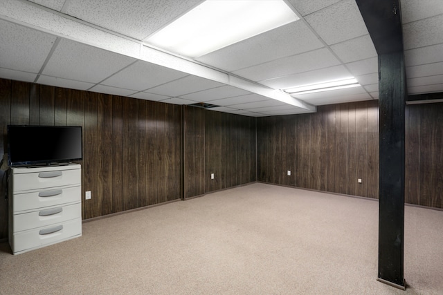 basement featuring a drop ceiling, light colored carpet, and wood walls