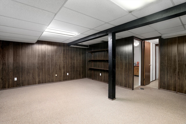 basement featuring light colored carpet, a drop ceiling, and wood walls