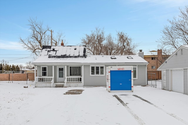 snow covered house featuring a porch and a garage