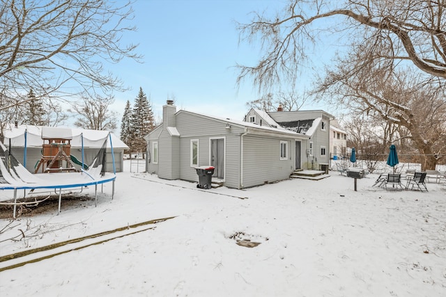 snow covered back of property with a playground and a trampoline