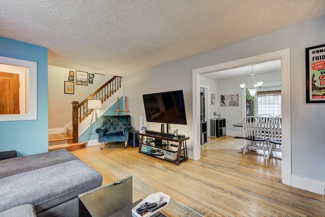 living room with wood finished floors, a textured ceiling, an inviting chandelier, and stairs