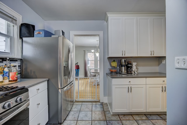 kitchen with appliances with stainless steel finishes, white cabinets, a notable chandelier, and light tile patterned flooring