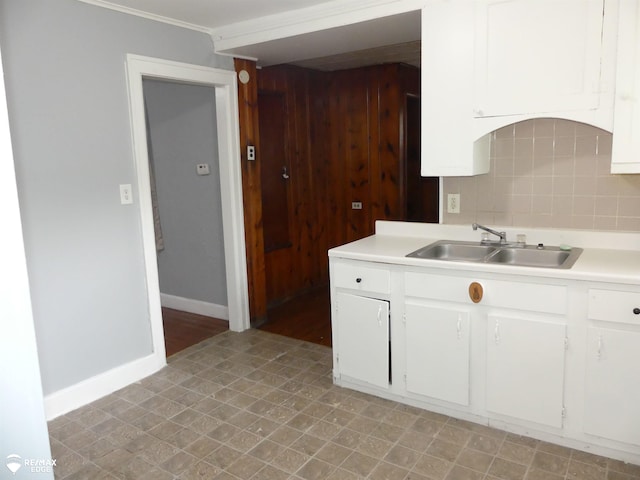 kitchen featuring sink, crown molding, wooden walls, white cabinets, and decorative backsplash