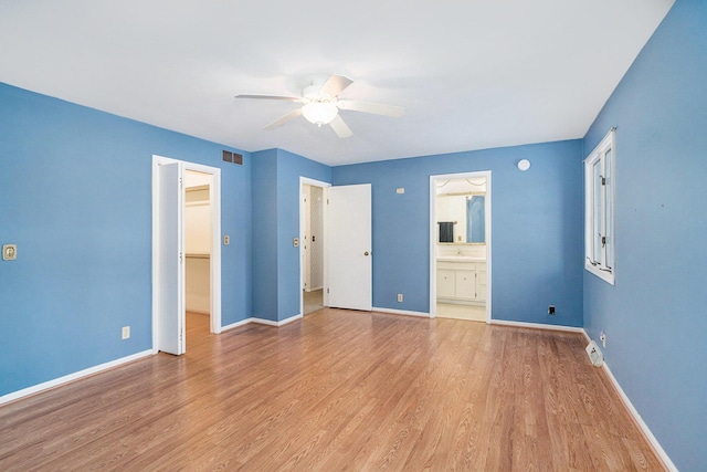 unfurnished bedroom featuring ensuite bathroom, a walk in closet, ceiling fan, and light hardwood / wood-style flooring