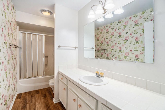 full bathroom with hardwood / wood-style flooring, bath / shower combo with glass door, vanity, and toilet