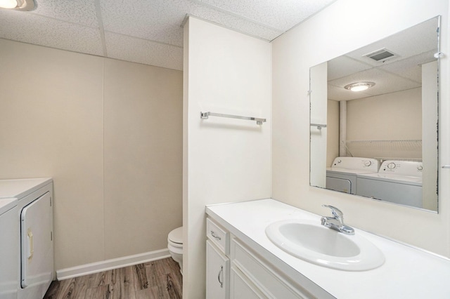 bathroom with hardwood / wood-style flooring, a paneled ceiling, washer and dryer, and toilet