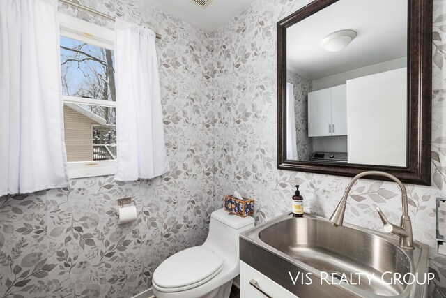 bathroom with toilet, wallpapered walls, and vanity