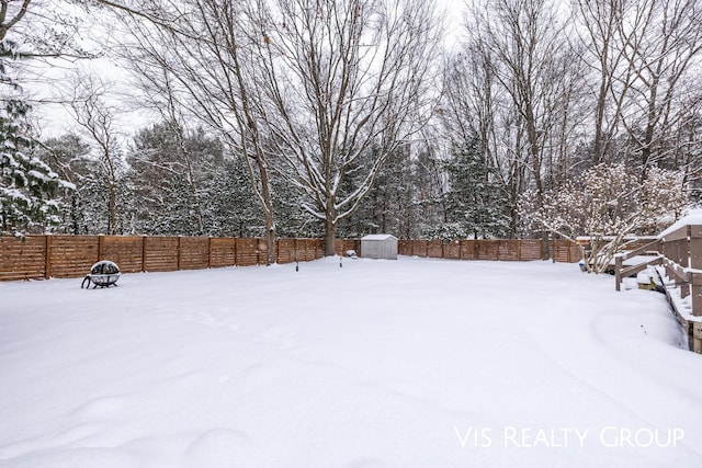 yard covered in snow featuring a storage shed, a fenced backyard, and an outdoor structure