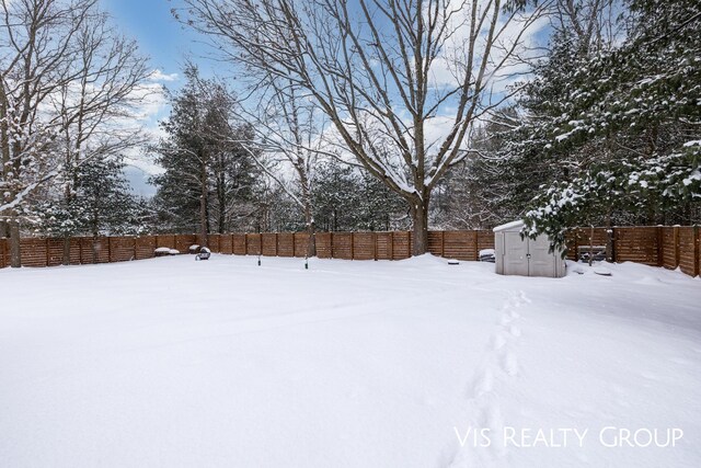 snowy yard featuring a fenced backyard, an outdoor structure, and a shed