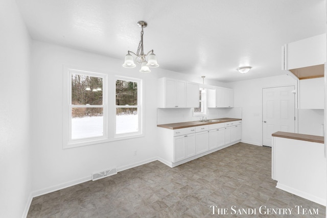 kitchen featuring butcher block counters, sink, white cabinetry, an inviting chandelier, and pendant lighting