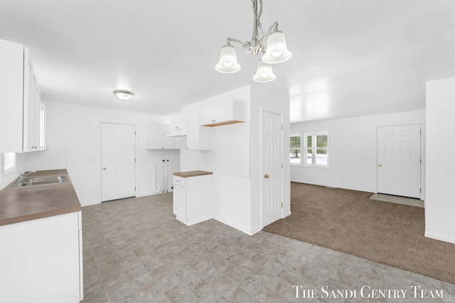 kitchen featuring white cabinetry, sink, hanging light fixtures, a notable chandelier, and light carpet