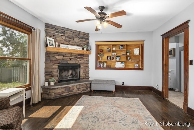 living room featuring a stone fireplace, dark wood-type flooring, and ceiling fan