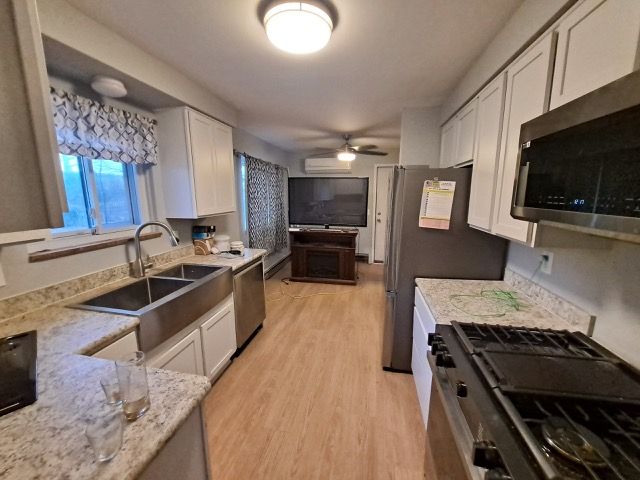 kitchen featuring sink, light hardwood / wood-style flooring, stainless steel appliances, light stone countertops, and white cabinets