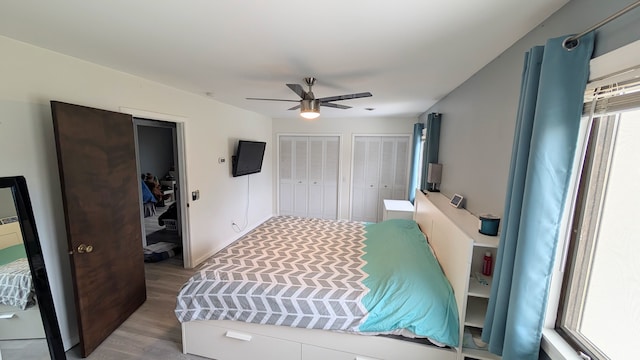 bedroom featuring ceiling fan, wood finished floors, and multiple closets