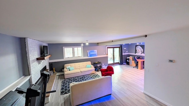 living area featuring a baseboard heating unit, a fireplace, baseboards, and wood finished floors