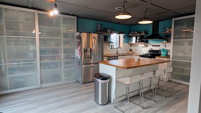 kitchen featuring wood counters, appliances with stainless steel finishes, a breakfast bar, light wood-type flooring, and open shelves