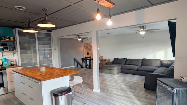 interior space with white cabinets, butcher block countertops, open floor plan, a center island, and light wood-style floors