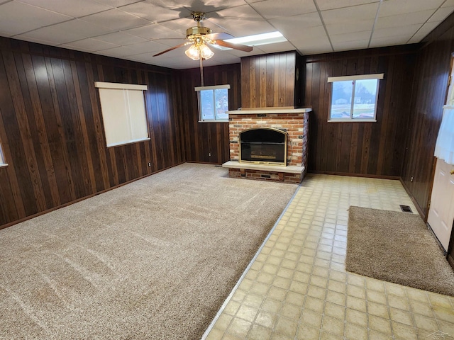 unfurnished living room with ceiling fan, a healthy amount of sunlight, a fireplace, and wood walls