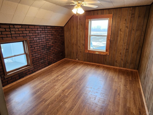 additional living space featuring vaulted ceiling, brick wall, wood walls, wood-type flooring, and ceiling fan