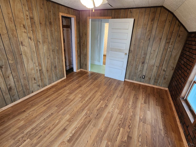 unfurnished bedroom featuring lofted ceiling, baseboard heating, hardwood / wood-style floors, wooden walls, and a textured ceiling